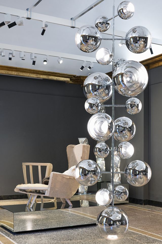 a chandelier with man metallic orbs sits before a wingback chair on a pedestal