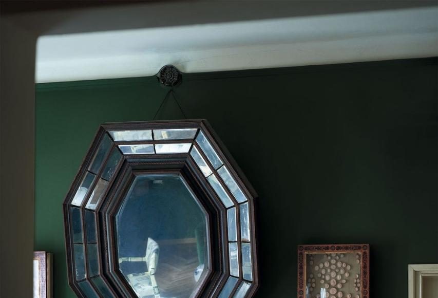 a fireplace in a room with tufted leather sofa and art deco mirror over the mantel filled with objects