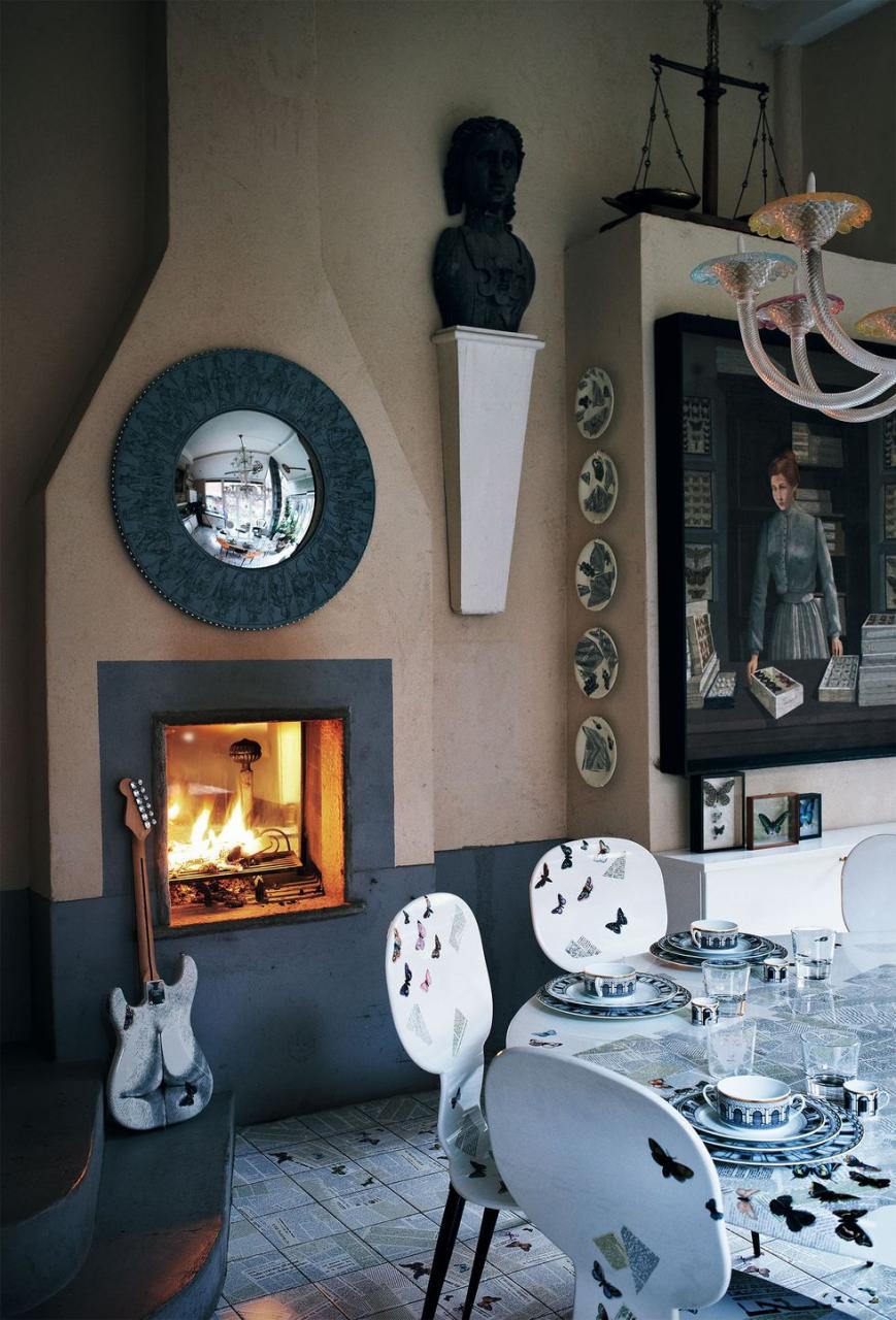 dining table with chairs all white with colorful butterfly shapes and a wall full of round and shaped mirrors and an inset fireplace with a guitar nearby