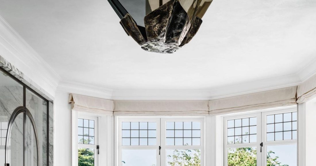 rounded bathroom with double windows in an arc at the back with a standalone marble tub at center and a floating marble vanity and a large bat like light fixture at center and a glass shower at left