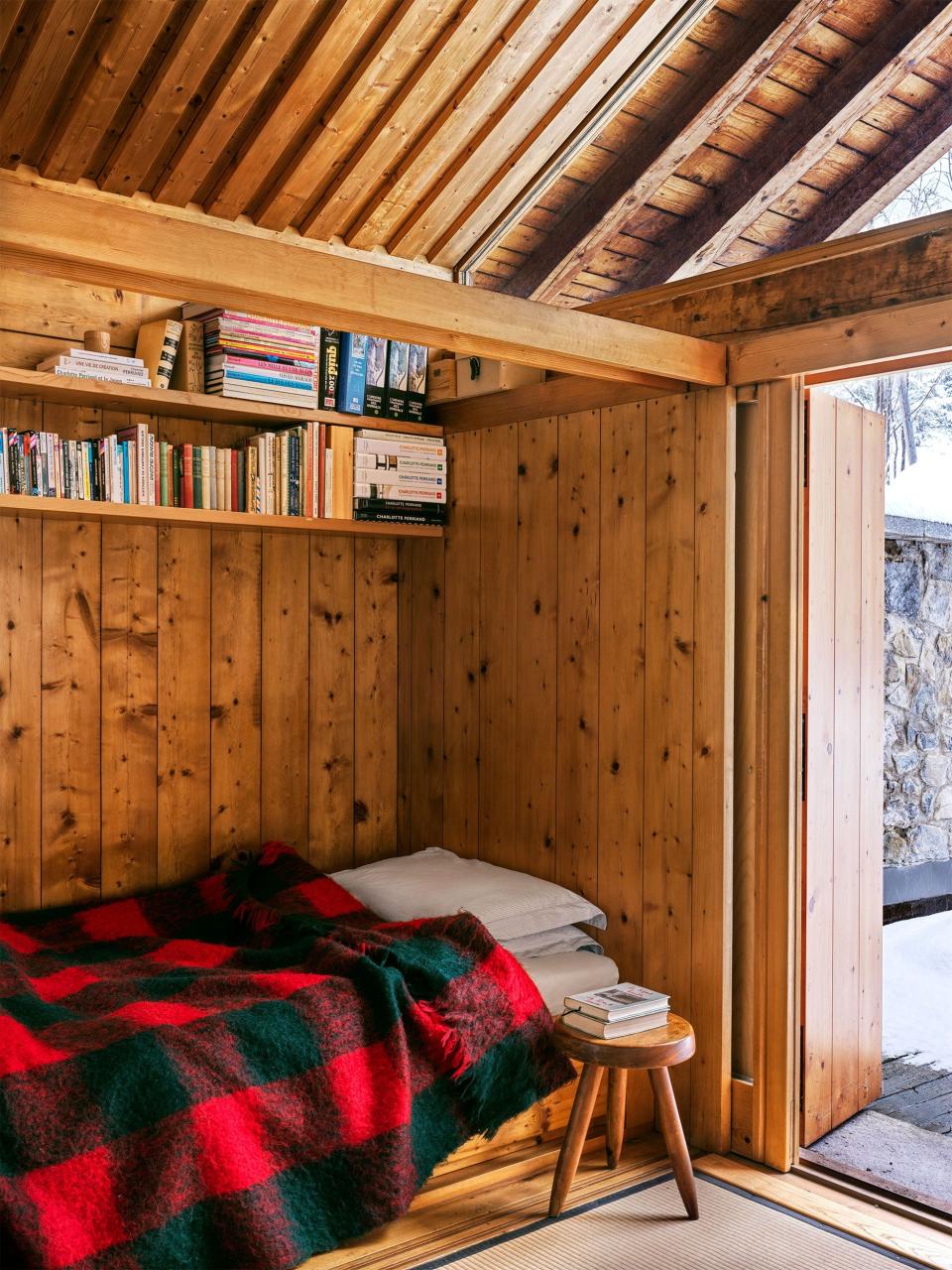 woode paneled nook with shelf for books and a red and black check blanket and a door leading outside