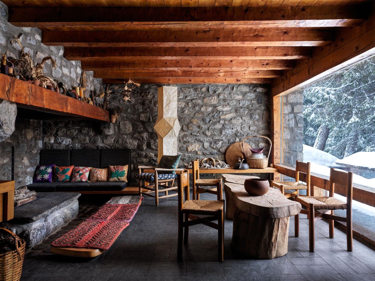 a room with a fireplace and chairs and beamed ceiling and pebbled gray stone walls