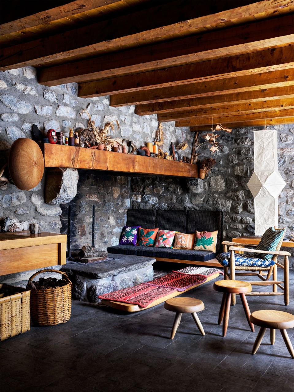 a room with a large hearth and beams and stone walls and simple wood furniture