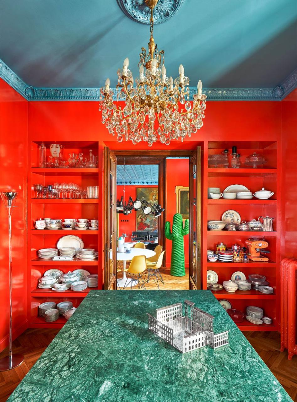 from the kitchen, a green marble countertop with built in shelves with dishware and glassware on either side of a door leading to a dining room with a large standing green cactus sculpture next to a table and chairs