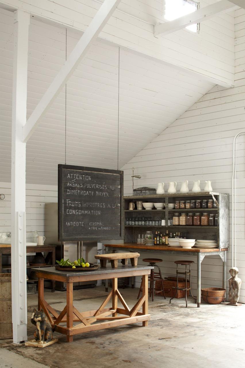 high ceilinged white barn with rustic table and large chalkboard hanging above it and various objects and sculptures scattered about