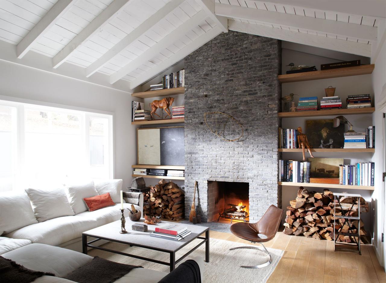 living area with white sofa and gray brick wall with inset fireplace and shelving and a pile of wood under it and a square cocktail table and small leather modern chair