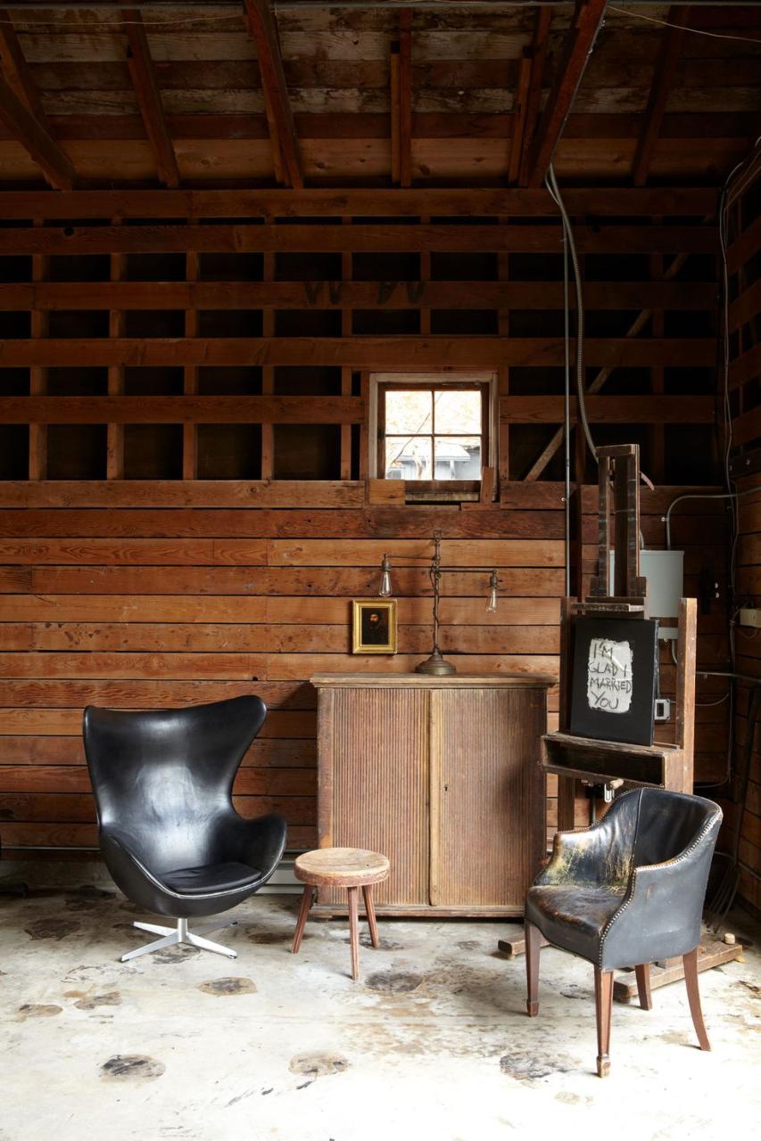 living area detail with a black leather egg chair with metal base and a worn out leather armchairs and a small stool and a rustic easel with a chalkboard and a piece of paper on which is written i'm glad i married you