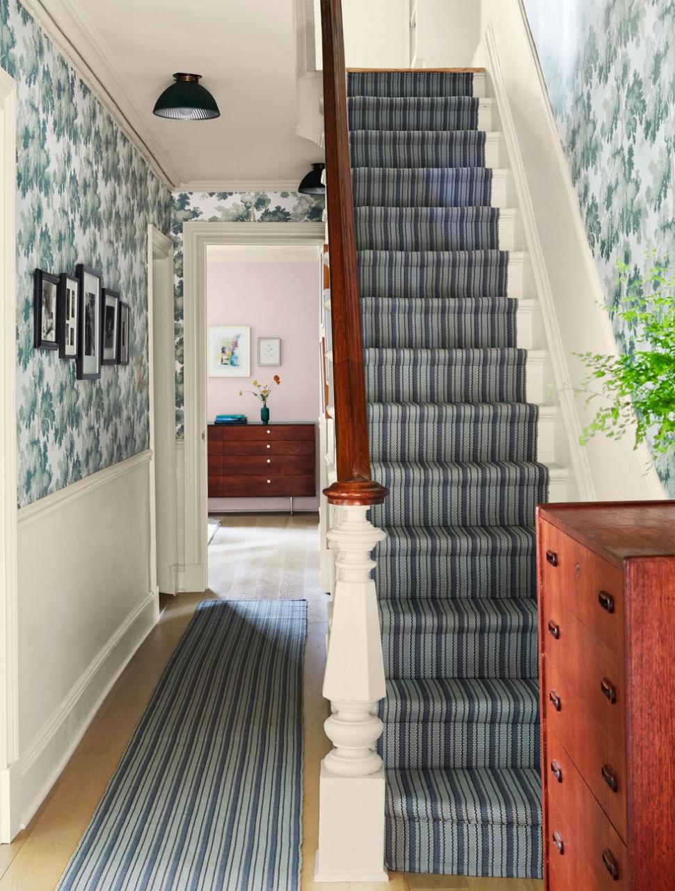 hallway with striped runner on floor and stairs leading up with matching striped fabric and on the walls is a very verdant wallpaper