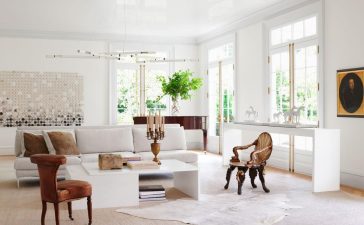 in a white living room is a white sofa, two side chairs, a white cocktail table with books and candelabra, white sideboard, a grand piano, white chandelier with brass arms, a large artwork on back wall, white carpet