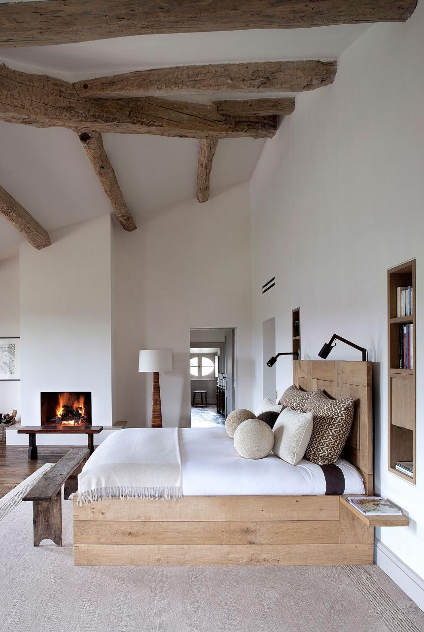 a bedroom with white walls and a few ceiling beams and a fireplace and simple platform bed