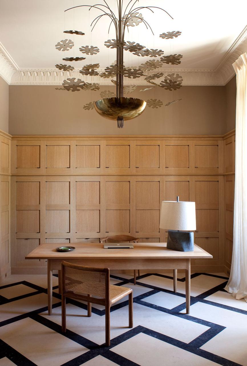 paneled office with a wood desk table and chair and geometric light and dark carpet and a metal bowl chandelier with cutout flowers