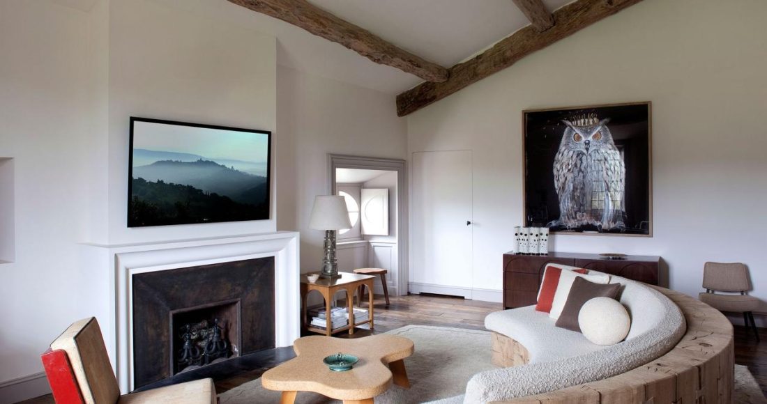 a seating area in a bedroom with a fireplace and curved sofa and red chair and large owl painting along the back wall