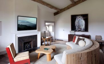 a seating area in a bedroom with a fireplace and curved sofa and red chair and large owl painting along the back wall