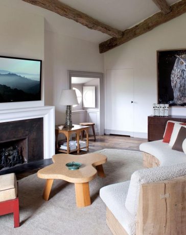 a seating area in a bedroom with a fireplace and curved sofa and red chair and large owl painting along the back wall