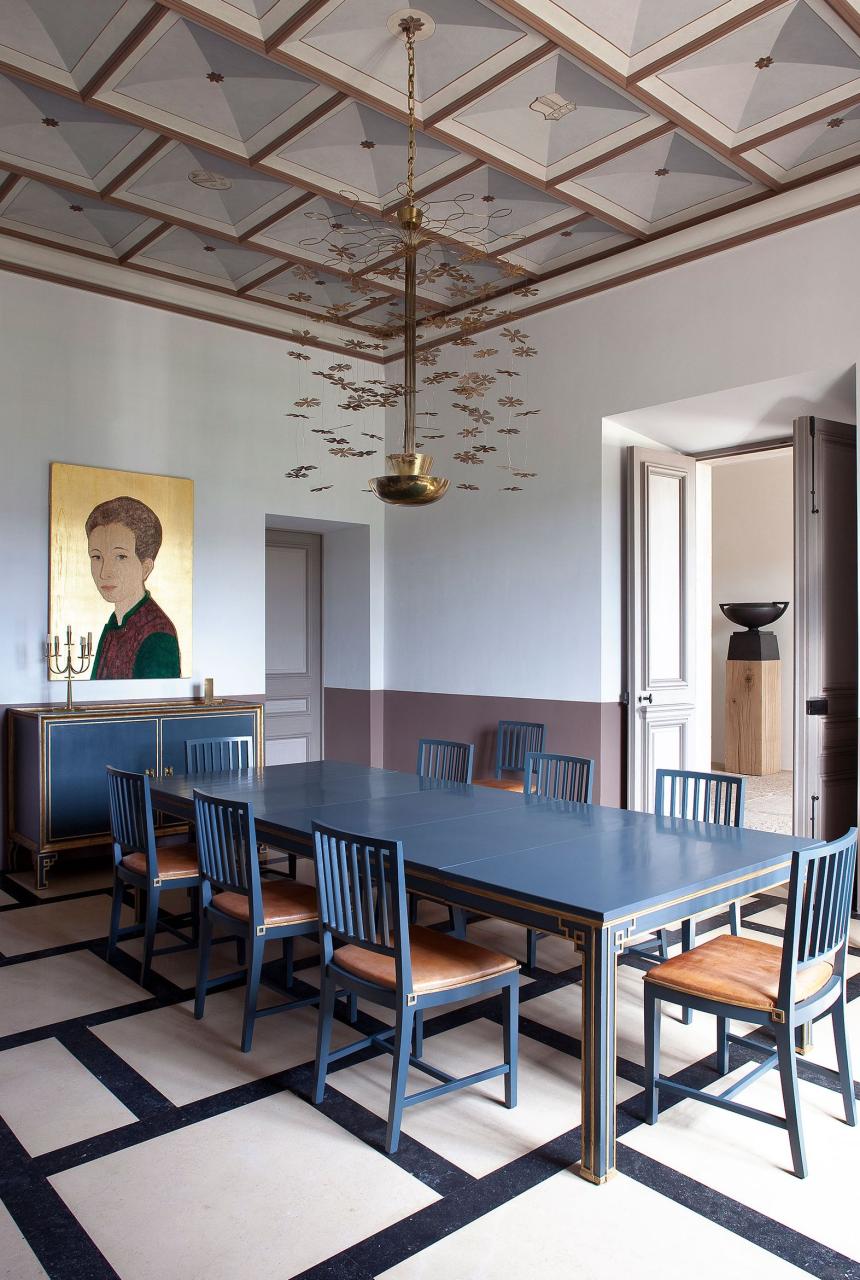 a dining room with blue table and chairs a chandelier overhead and a modern colorful portrait on the wall behind