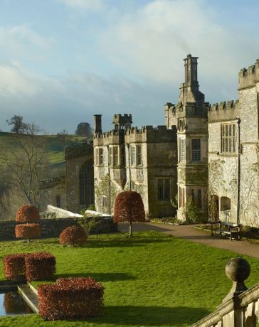 a large english manor building made of stone with a extensive lawn in front of it