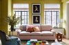 a living room with a pink sofa and a coloful glass coffee table and a blue and white armchair and tall french doors at the back and chartreuse painted walls