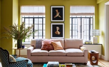 a living room with a pink sofa and a coloful glass coffee table and a blue and white armchair and tall french doors at the back and chartreuse painted walls