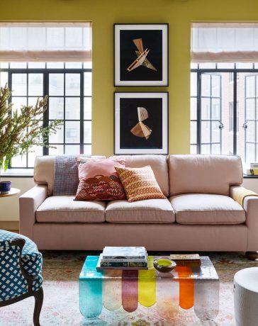 a living room with a pink sofa and a coloful glass coffee table and a blue and white armchair and tall french doors at the back and chartreuse painted walls