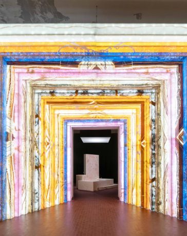 an archway made of colorful stone that leads to a pink marble bathtub installation