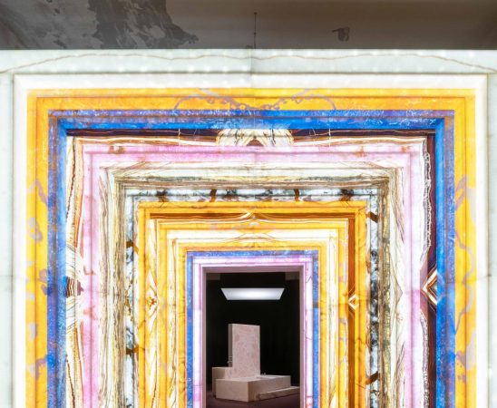 an archway made of colorful stone that leads to a pink marble bathtub installation